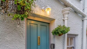 A blue door with a brass handle, a wall-mounted light fixture, and a hanging flower pot. - 4 Bed in Tenby (oc-fb042) (Tenby)