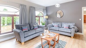 Ein geräumiges Wohnzimmer mit zwei grauen Sofas, einem Holztisch und einem großen Fenster mit Vorhängen.