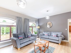 Ein geräumiges Wohnzimmer mit zwei grauen Sofas, einem Holztisch und einem großen Fenster mit Vorhängen.