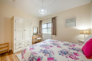 Une chambre à coucher avec un grand lit, une armoire, un bureau avec un miroir et une fenêtre avec des rideaux.