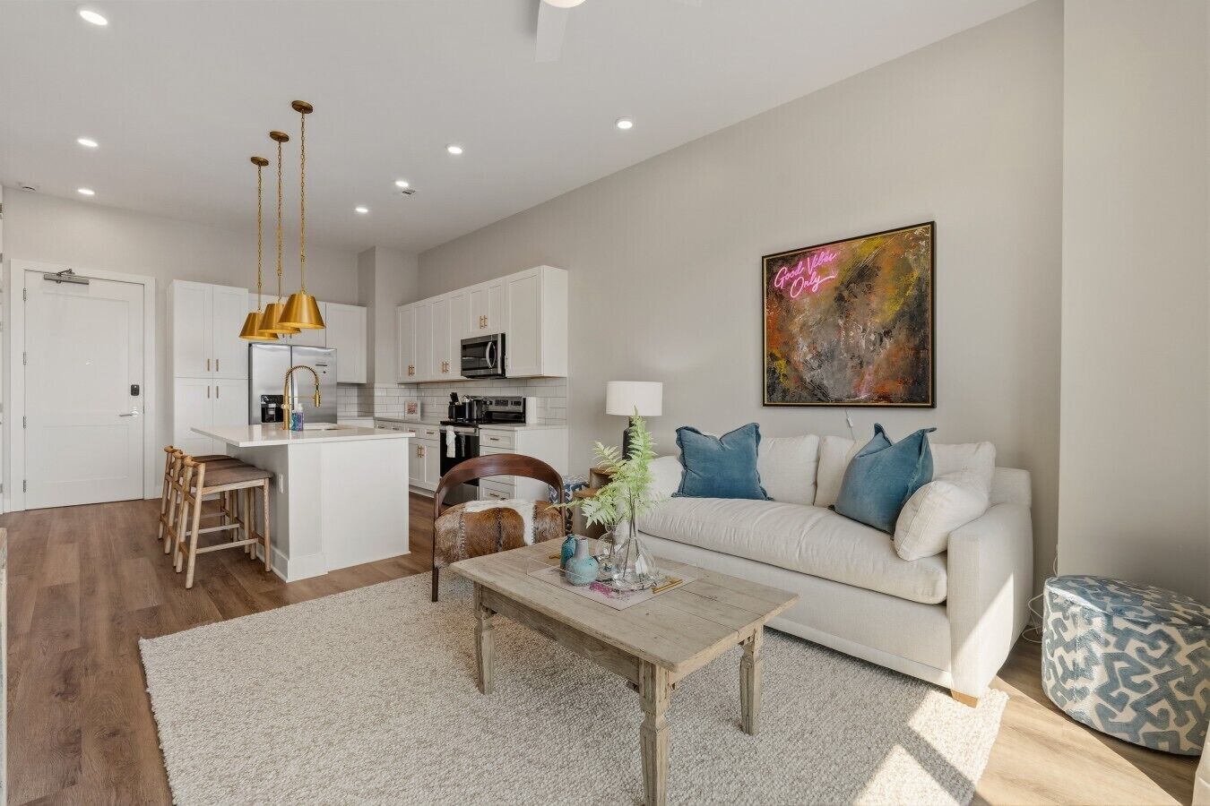 A modern living room with a sofa, coffee table, and a kitchen area with white cabinets and a pendant light.