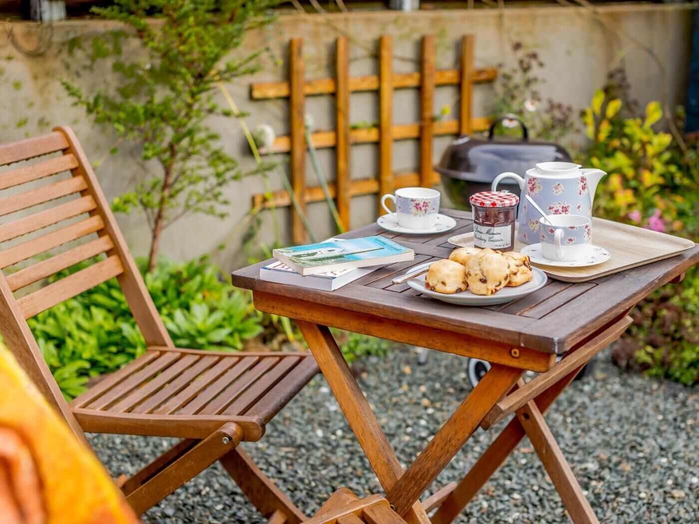 Uma mesa de madeira com um livro, um prato de biscoitos e duas chávenas com pires.