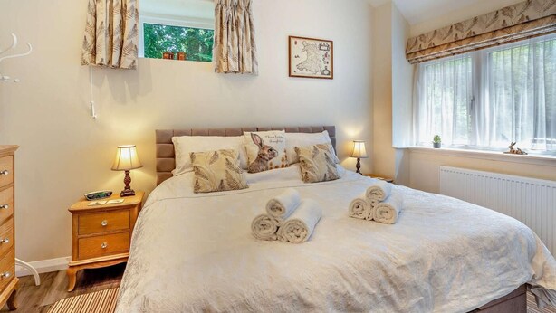 Een slaapkamer met een bed, twee nachtkastjes, een kast, een raam met gordijnen, een kaart aan de muur en een kleine plant op de vensterbank.