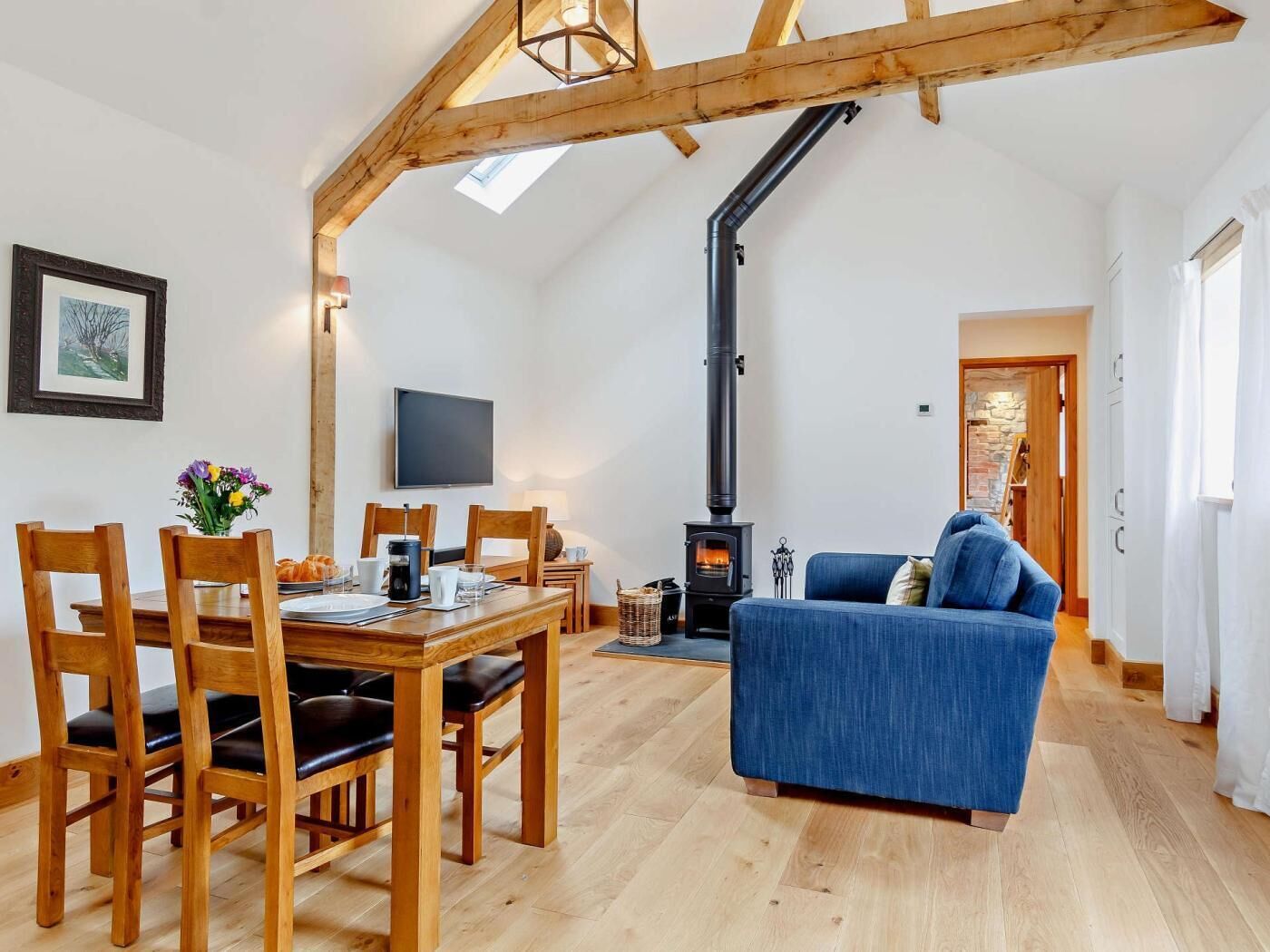 Een gezellige woonkamer met een houten eettafel, een blauwe bank en een open haard.
