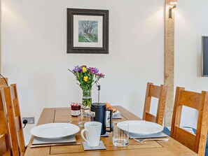 Ein Esstisch mit Tellern, einer Tasse, einem Glas, einer Blumenvase, einer Kerze und einem gerahmten Bild an der Wand.
