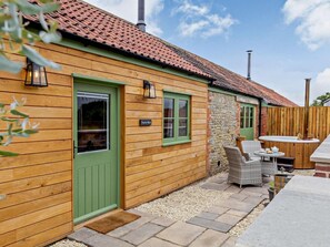 Ein Holzhaus mit grüner Tür, einer Steinsäule und einer Terrasse mit Gartenmöbeln.