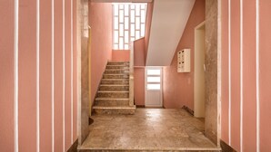 Ein schmaler Korridor mit Treppe, einer Tür am Ende und einem Fenster mit geometrischem Muster.