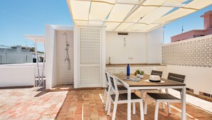 Eine Dachterrasse mit Esstisch, Stühlen, einer Dusche und einer Wand mit Muster.