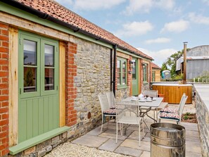 A stone building with green shutters, a patio with metal chairs and a table, and a hot tub. - 2 Bed in Taunton (oc-80694) (North Curry)