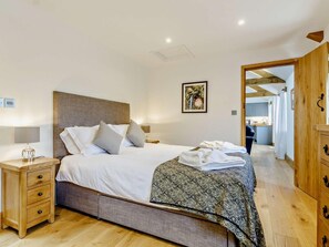 A bedroom with a bed, bedside tables, a nightstand, a wooden wardrobe, and a kitchen visible in the background. - 2 Bed in Taunton (oc-80694) (North Curry)