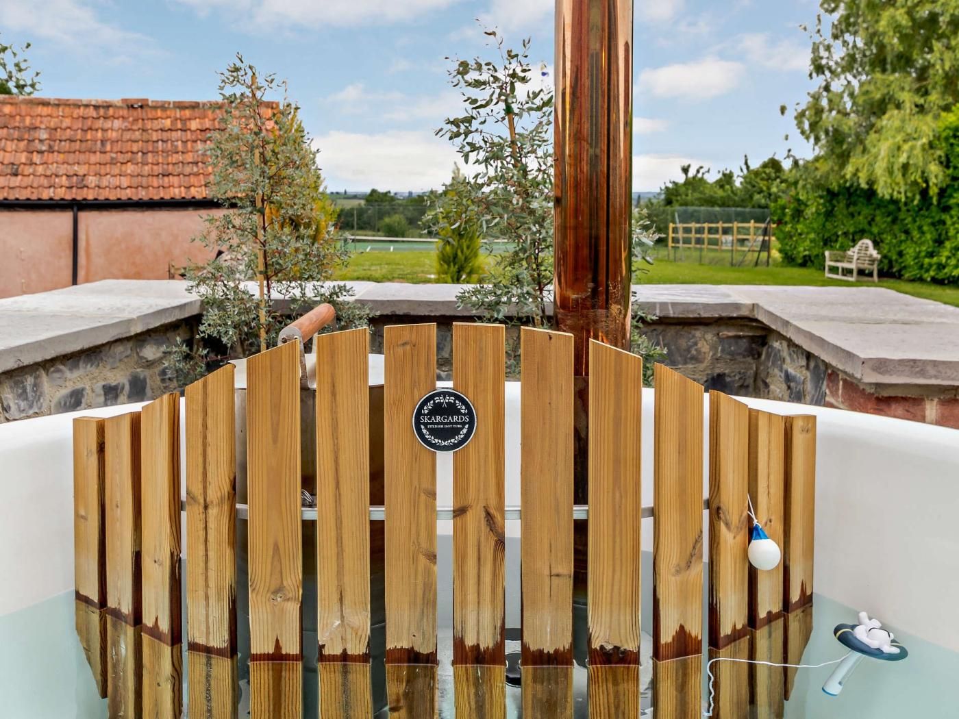 A wooden gate with a sign, a pool, and a view of a garden and buildings.