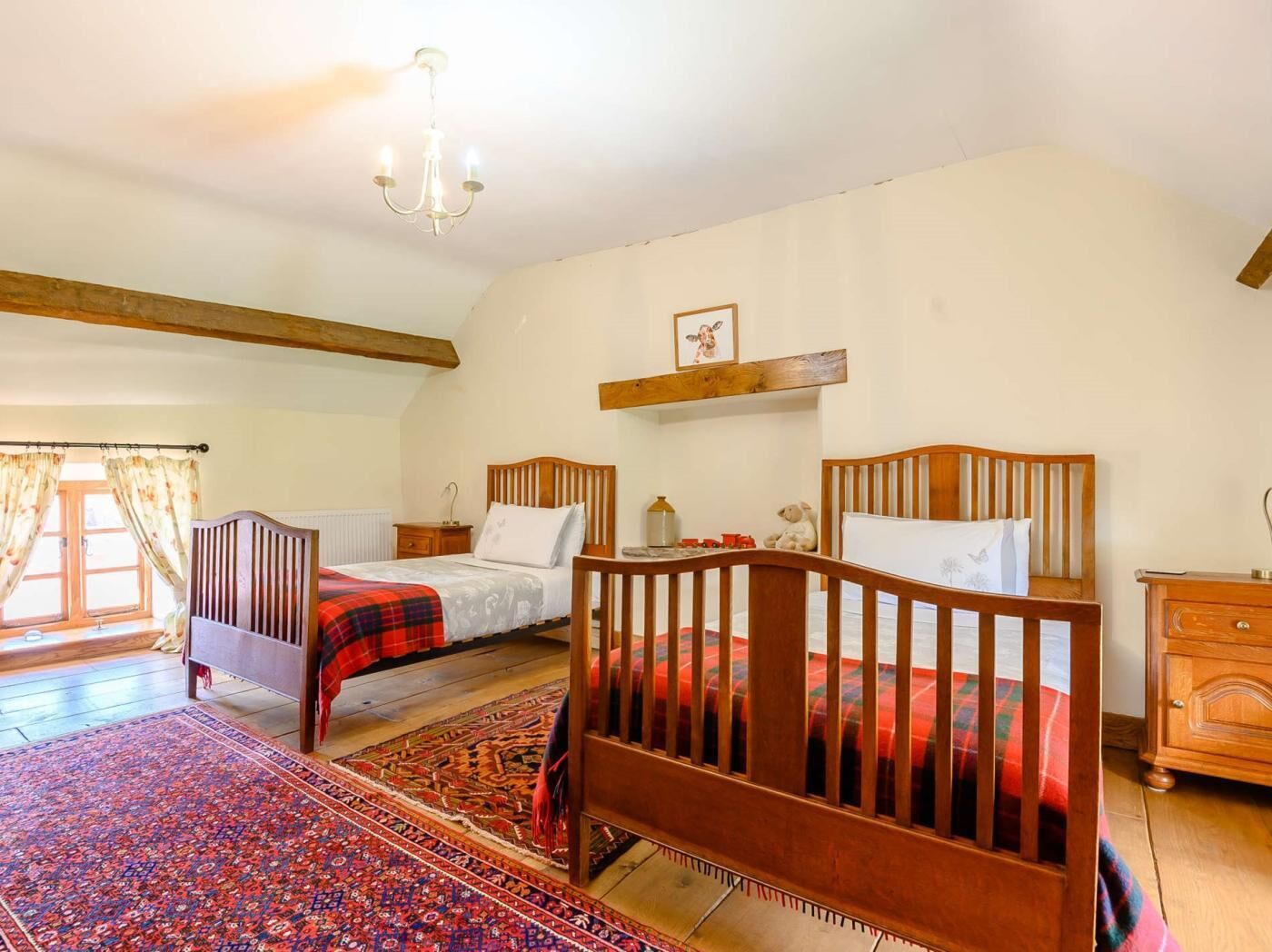 Une chambre à coucher avec deux lits en bois, un lustre, une commode en bois et un tapis à motifs.
