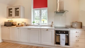 Eine moderne Küche mit weißen Schränken, einem eingebauten Backofen, einer Mikrowelle und einem Fenster mit rotem Rollo.