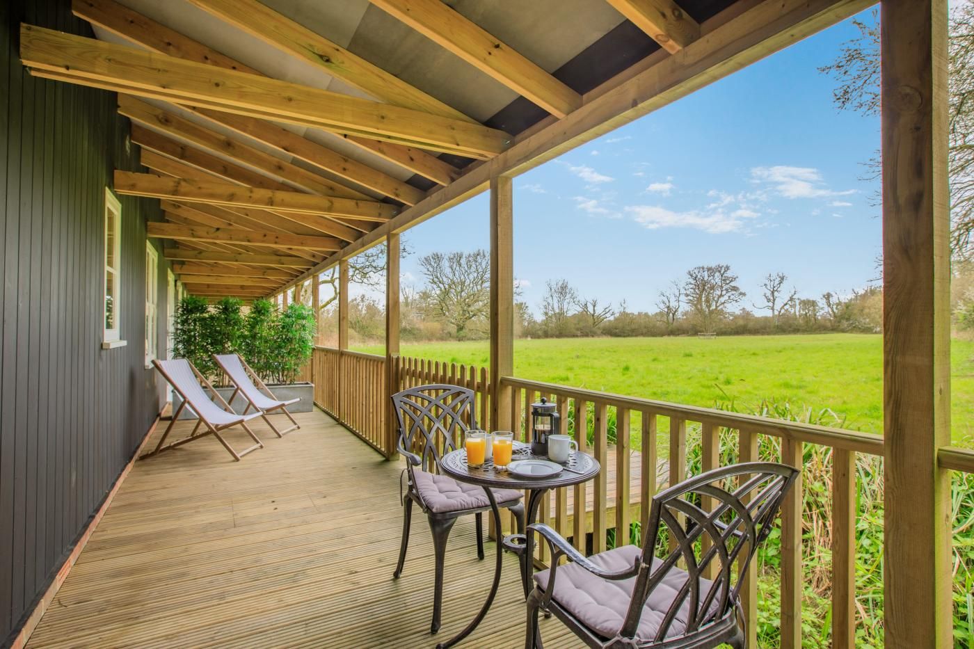 A covered outdoor area with a table and chairs, a view of a green field, and a wooden deck.