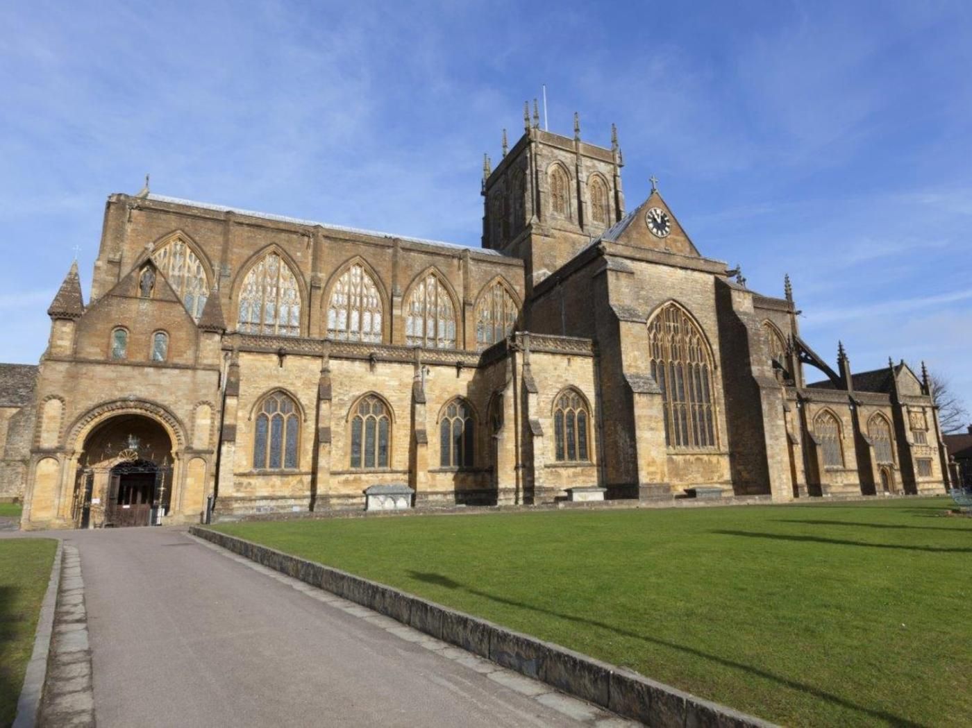A historic building with a large arched entrance, a prominent clock tower, and a well-maintained lawn in front.