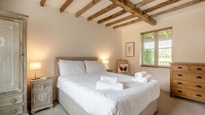 Ein Schlafzimmer mit einem Bett, Nachttischen, einer Kommode, einem Fenster mit Jalousien und einer Holzbalkendecke.
