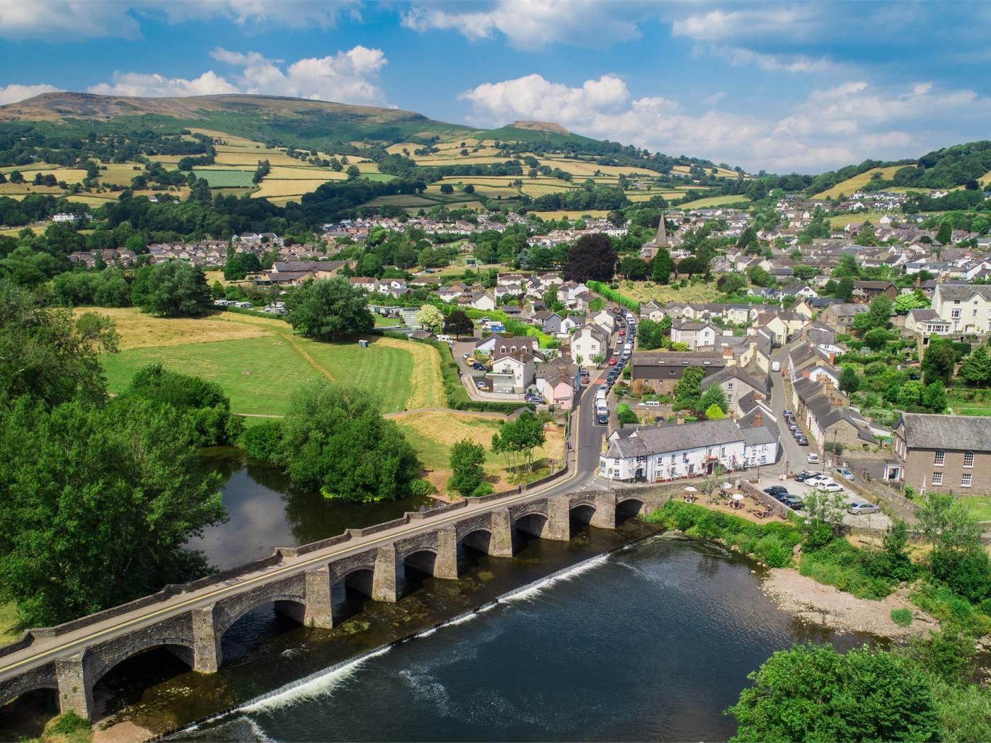 A river with a bridge, a town with houses, and green fields.