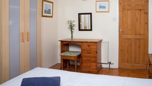 Ein Schlafzimmer mit einem Bett, einem Holztisch mit Stuhl, einem Kleiderschrank und einer Tür.