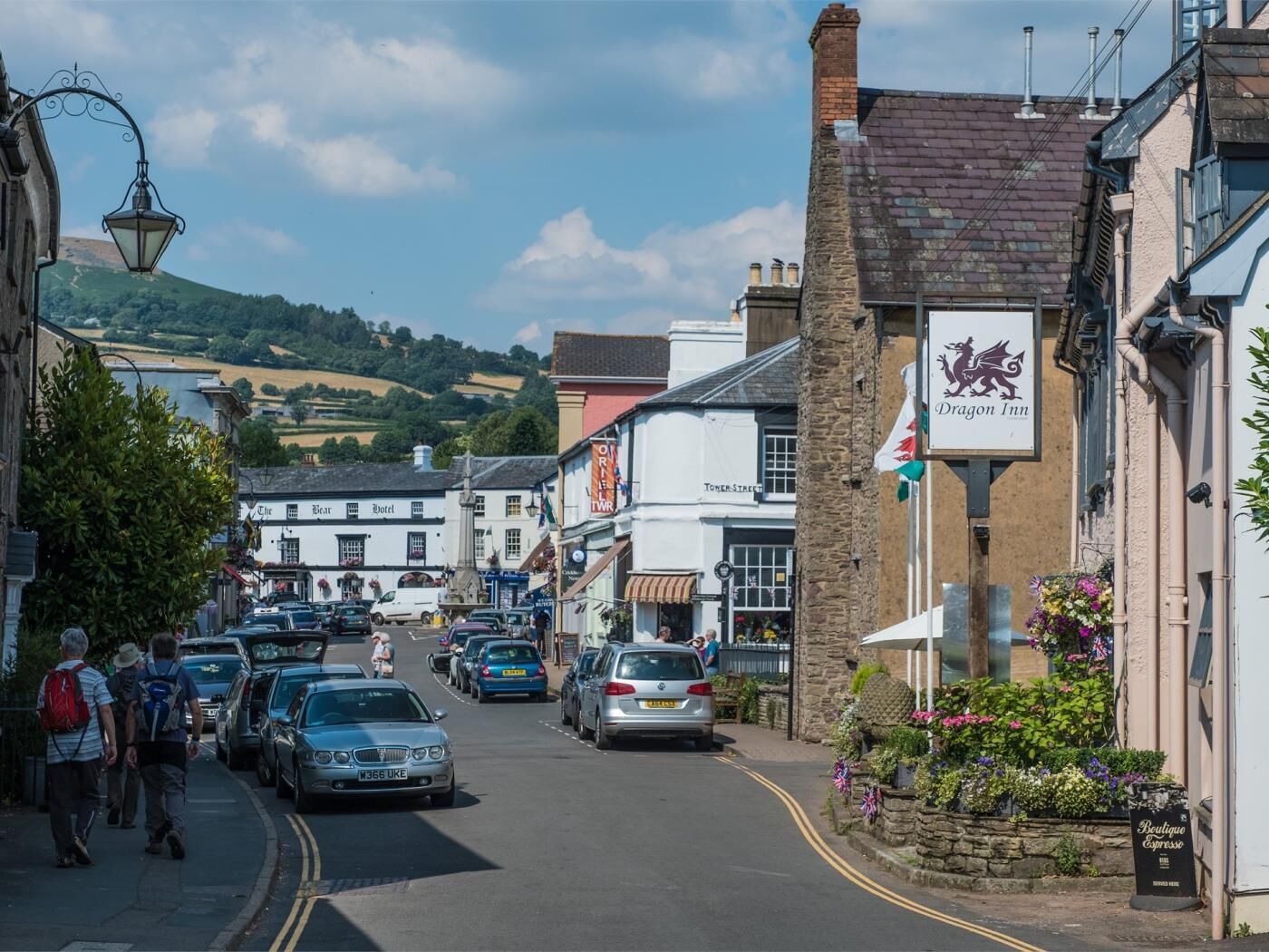 Une vue de rue avec des voitures garées, une enseigne indiquant un hôtel appelé « Dragon Inn », et un café proposant des expressos de qualité.