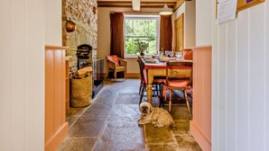 A cozy kitchen with a stone fireplace, wooden beams, a dining table set for four, and a dog lying on the floor. - 4 Bed in Hay-on-wye (oc-bn116) (Hay-on-Wye)