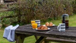 A picnic setup with croissants, juice, and a coffee maker on a wooden table. - 1 Bed in Ystradgynlais (oc-bn046) (Ystradgynlais)