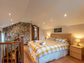 Ein Schlafzimmer mit Steinwand, einem hölzernen Bett, einem Nachttisch und einer Treppe.