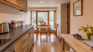 A kitchen with wooden cabinets, a dining table with chairs, and a view through the glass door. - 1 Bed in Ystradgynlais (oc-bn046) (Ystradgynlais)