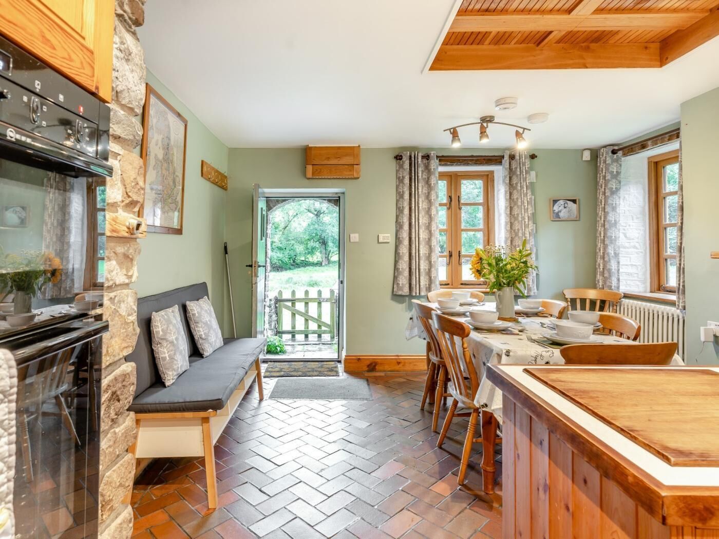 A cozy kitchen with a stone wall, wooden ceiling, and a dining area with a table set for four.