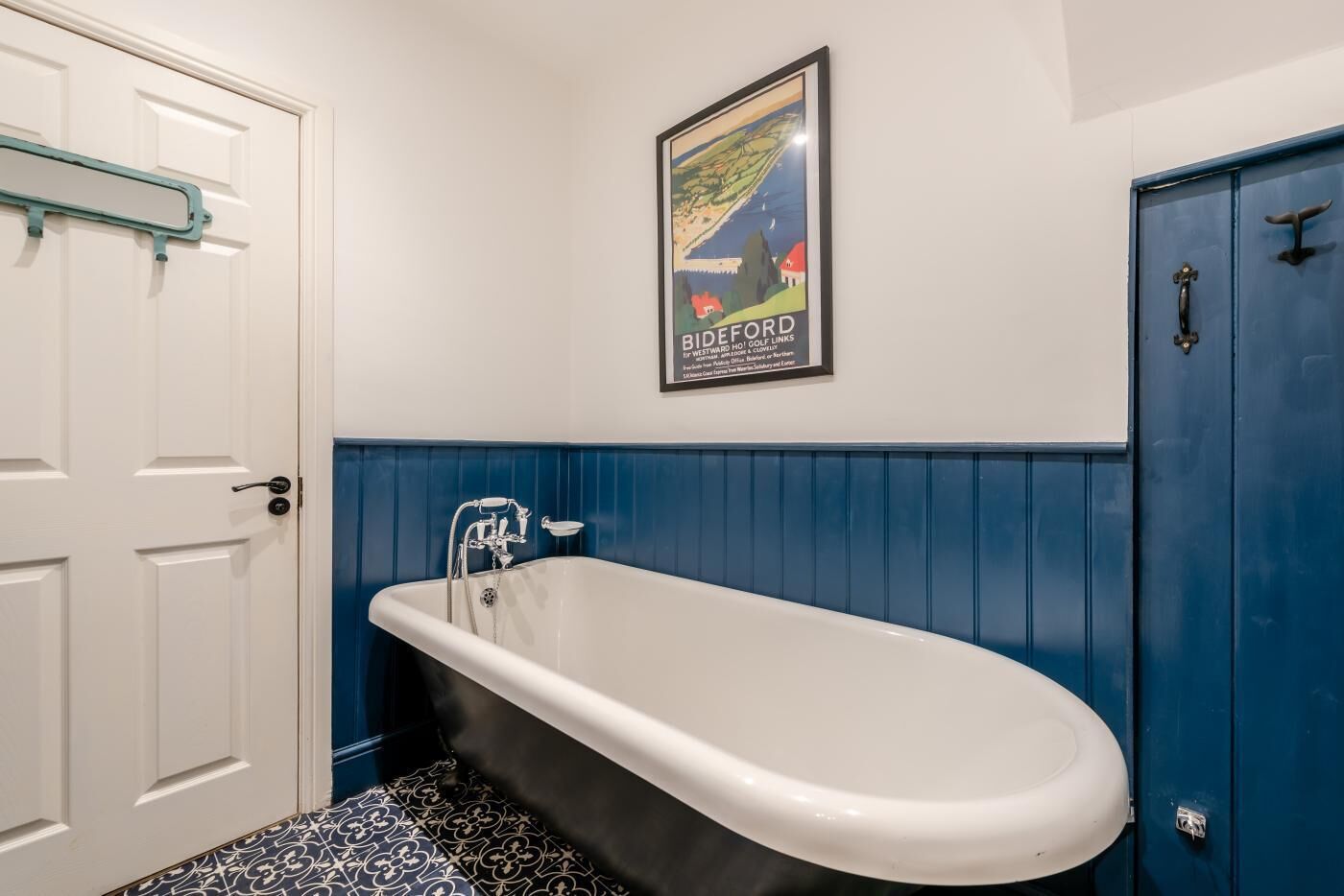 A bathroom with a white door, a blue bathtub, and a poster on the wall.