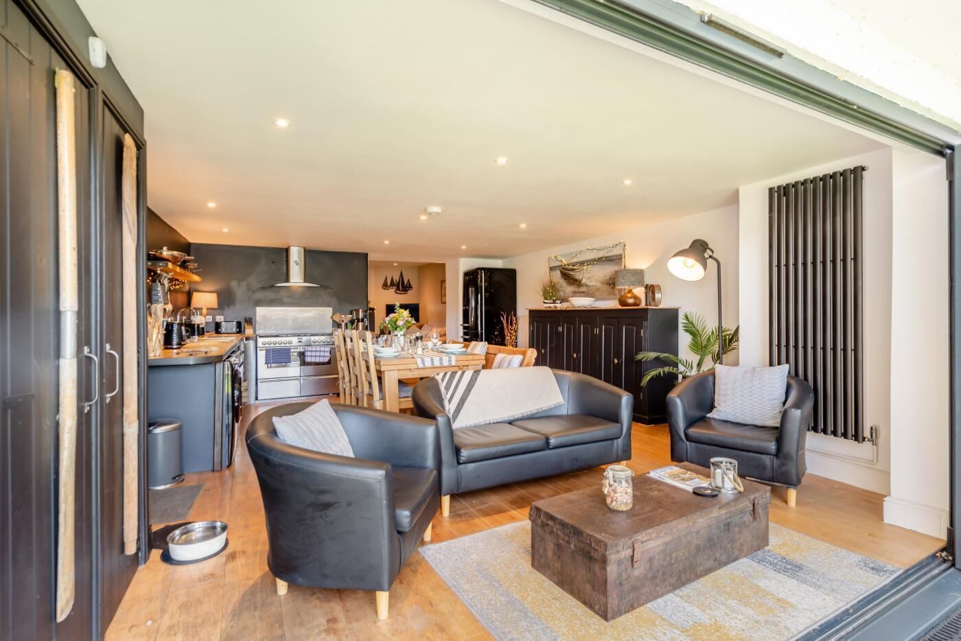 A modern living room with a sofa, chairs, a coffee table, and a kitchen area in the background.