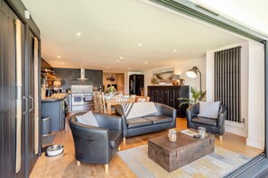 A modern living room with a sofa, chairs, a coffee table, and a kitchen area in the background.