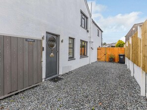 A white building with a grey door, a wooden gate, and a gravel driveway.