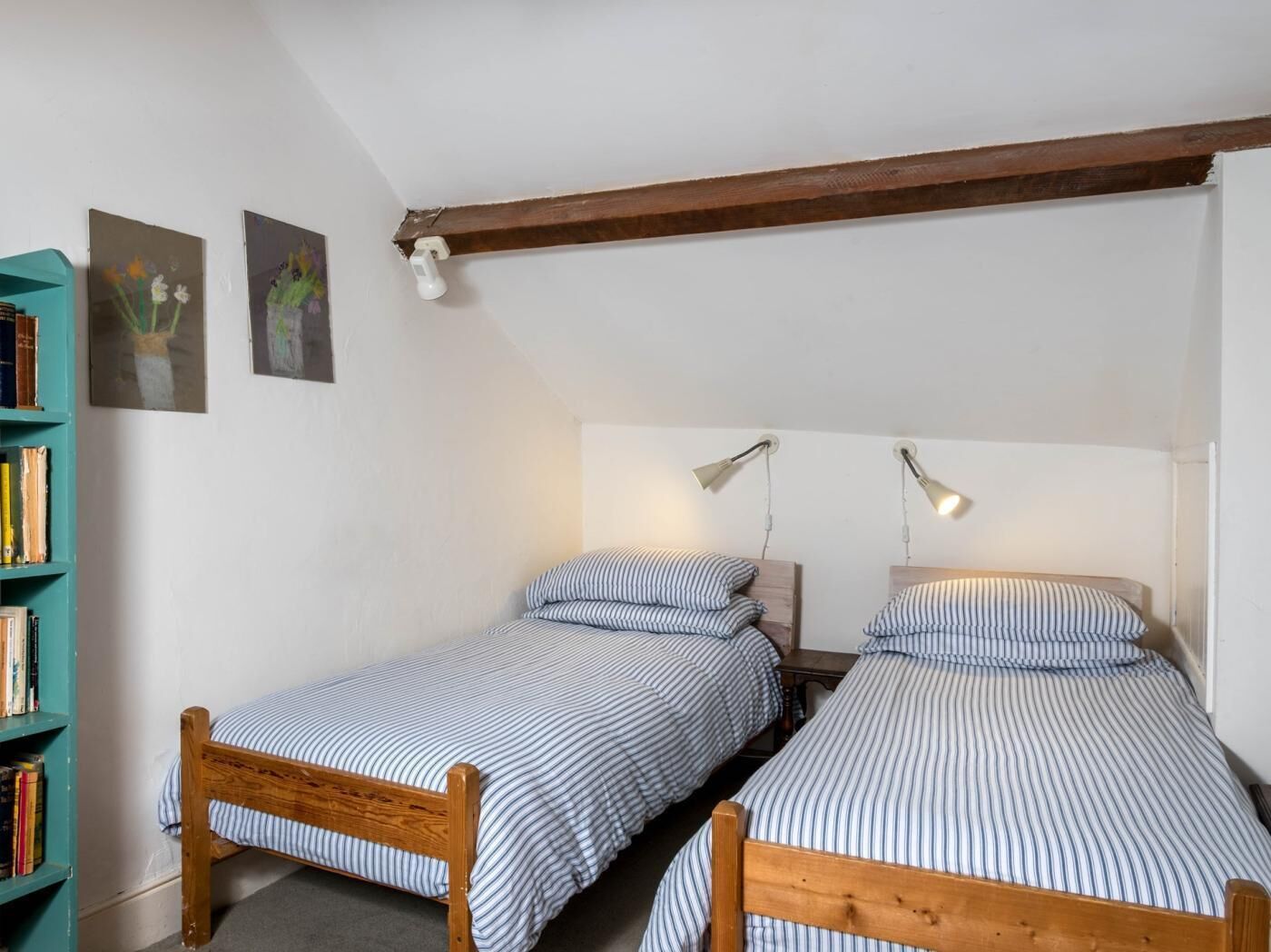 Um quarto pequeno e aconchegante com duas camas de solteiro, uma estante de livros e duas luminárias.