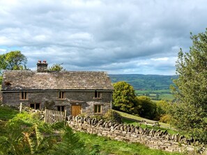 Ein Haus aus Stein mit einem geneigten Dach, einer Holztür und einer Mauer davor.