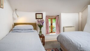 Un dormitorio con dos camas, una ventana con cortinas, una mesita de noche con un jarrón y un radiador.