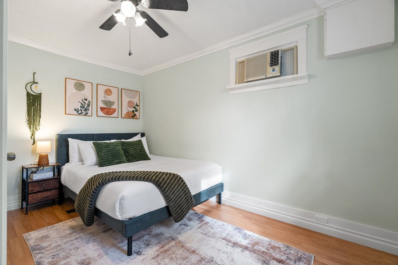 A bedroom with a bed, bedside table, lamp, wall art, and a ceiling fan.