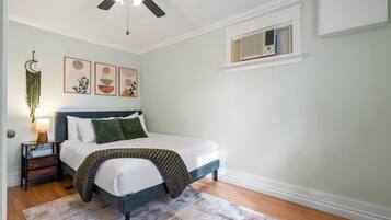 A bedroom with a bed, bedside table, lamp, wall art, and a ceiling fan.