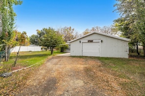 A single-story building with a garage door, surrounded by a grassy area with trees and a gravel path leading to it.