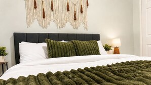 A bed with a dark headboard, white bedding, and a green textured throw blanket. - The Badlands Basecamp (Drumheller)