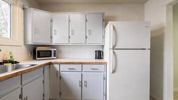 A kitchen with grey cabinets, a microwave, a refrigerator, and a wooden countertop.