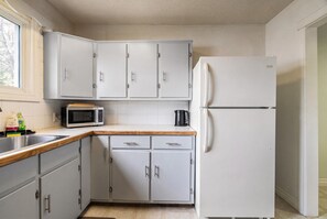 A kitchen with grey cabinets, a microwave, a refrigerator, and a wooden countertop. - The Badlands Basecamp (Drumheller)