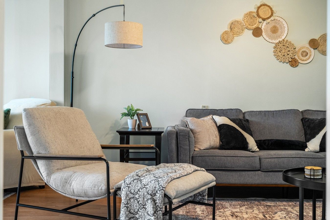 A modern living room with a grey sofa, a beige armchair, a patterned throw, a floor lamp, and a wall art piece.
