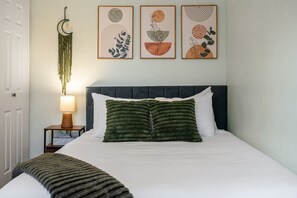 A neatly made bed with a dark headboard, a green throw blanket, and a wall-mounted decorative piece.