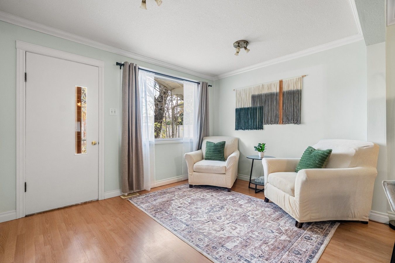 A room with two armchairs, a small table, a patterned rug, a door, and a window with curtains.