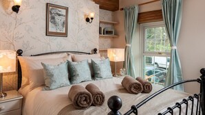 A bedroom with a bed, pillows, a bedside table, a lamp, a picture on the wall, and a window with curtains. - 2 Bed in Brecon (oc-bn181) (Talybont-on-Usk)