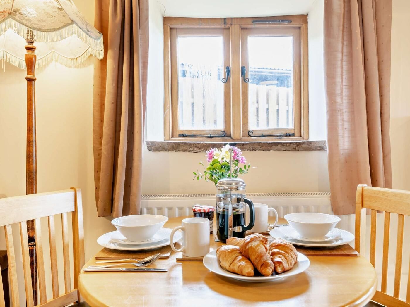 A breakfast table with croissants, coffee, and flowers.