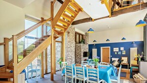 Une pièce spacieuse avec un escalier en bois, un coin repas avec des nappes bleues et un mur en pierre.