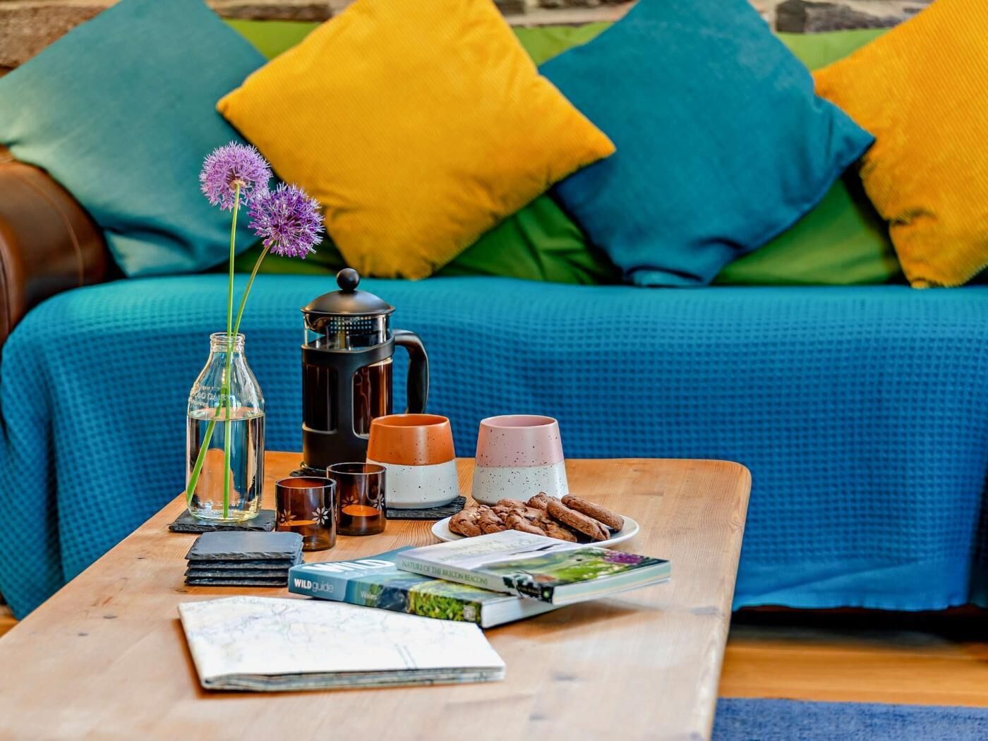 Un espacio de sala acogedor con una mesa de centro, libros, una cafetera y un plato de galletas.