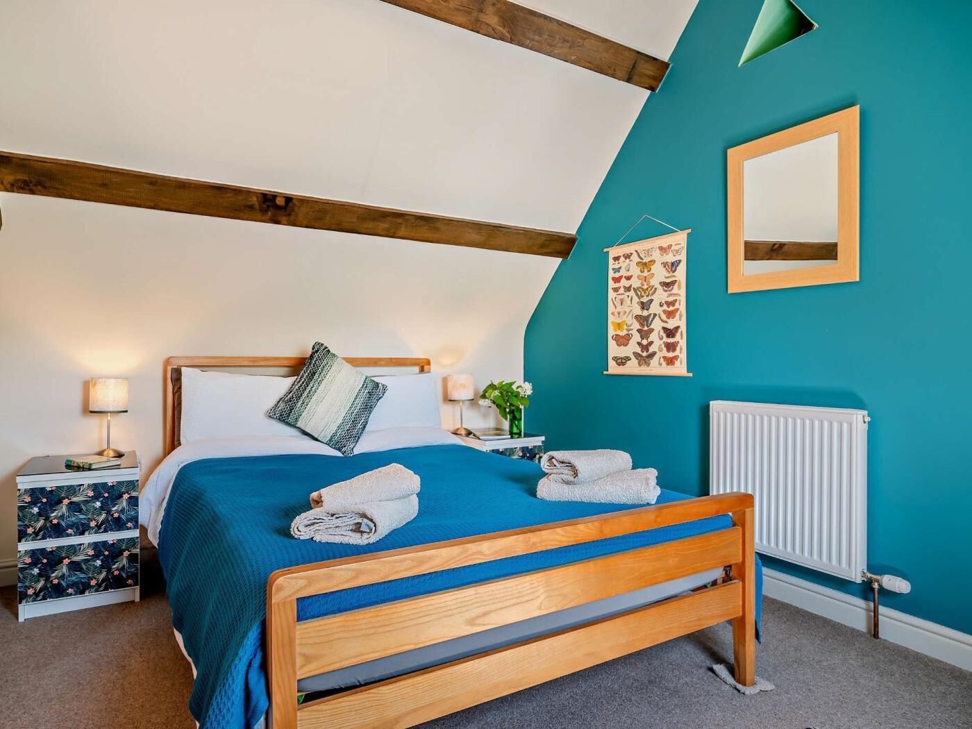 A bedroom with a bed, a nightstand, a wall-mounted mirror, and a radiator.