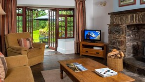 A cozy living room with a wooden sofa, a television, a fireplace, and a view of the outdoors. - 3 Bed in Llangadog (oc-bn223) (Llangadog)